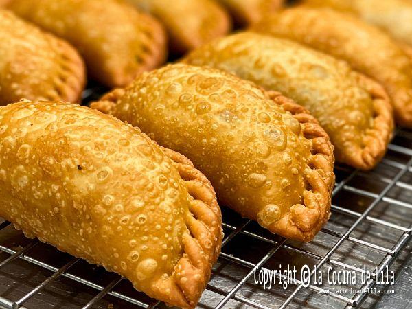 Empanadillas fritas doradas y crujientes sobre una rejilla de metal.