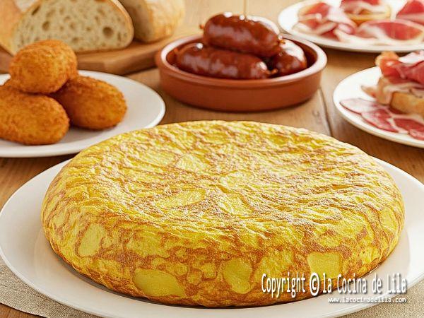 Imagen de una tortilla de papas española, dorada y de grosor uniforme, presentada en un plato blanco sobre una mesa rústica.